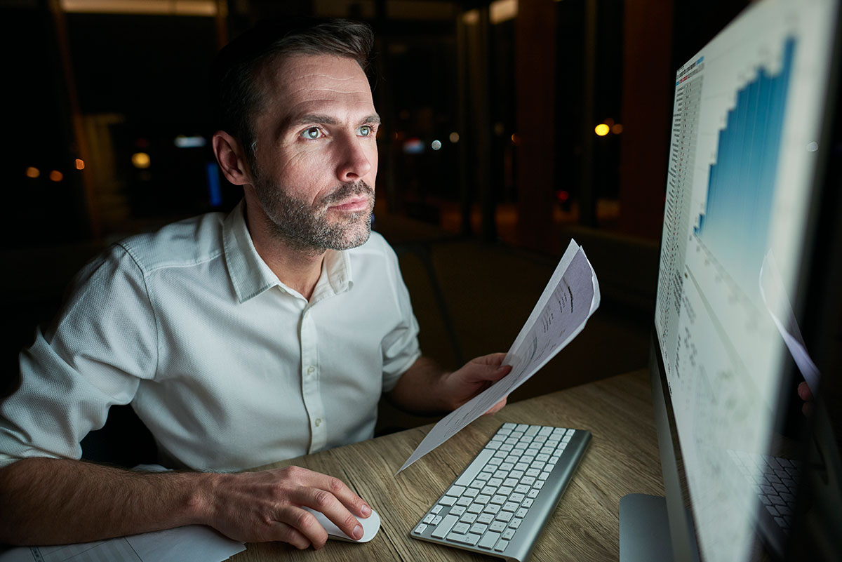 Focused man reviewing document while using computer